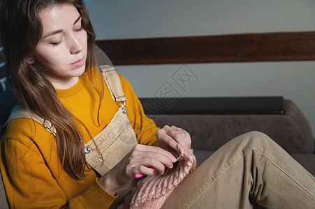 有吸引力的年轻女子坐在沙发上时编织羊毛衣 手织钩 家庭爱好生产天然羊毛制品女士女性快乐纤维手工工作纺织品活动工艺手指图片