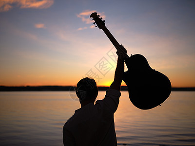 一个带着吉他的男人的背影 高高地看着粉红湖上的日落图片