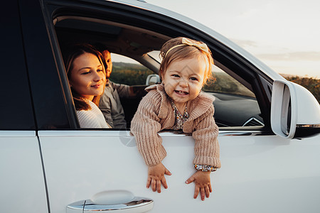 小女孩从车窗外看小女孩 年轻家庭与女婴在日落路途旅行背景图片
