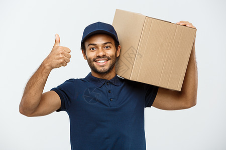 送货概念快乐的非洲裔美国人送货员拿着一个盒子包裹并出现重击的肖像 隔绝在灰色演播室背景 复制空间职业工作室男性男生城市商业邮政工图片