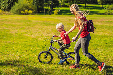 年轻母亲教她儿子如何在公园里骑自行车图片