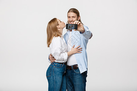 一对快乐的情侣拍自拍照片时 带着智能手机 在孤立的白色工作室背景上微笑技术恋人海滩房子冒充女孩公寓男性男人背景图片