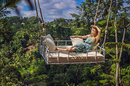 年轻女子在印度尼西亚巴厘岛的丛林雨林中荡秋千 在热带摇摆 秋千巴厘岛的潮流飞行女性女士太阳天空游客青少年吸引力棕榈假期图片