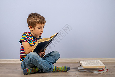 一个小男孩 在一摞书后面学习 看着一本日记 一个男孩坐在蓝色背景的地板上图片