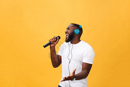 欢快积极 别致 英俊的非洲男子手持麦克风 头戴耳机听音乐唱歌 享受黄色背景中孤立的周末假期的肖像卷曲音乐播放器舞蹈技术乐趣女孩歌图片