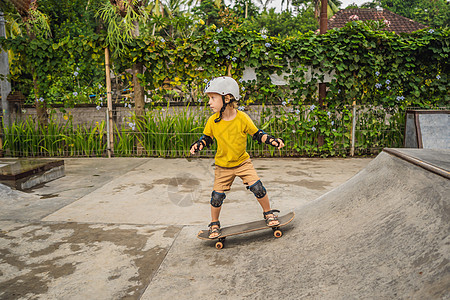 戴头盔和膝盖垫的体育男孩学会在滑板公园与滑板一起玩滑板长板童年太阳行动公园学习男性乐趣孩子闲暇图片