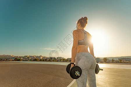 用哑铃拍背部的镜头 运动健壮的女孩用重量做健身锻炼 女人用耳铃在户外工作图片