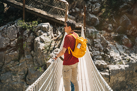 远足时 父子俩在山中的索桥上遥望 穿着随意的游客男童和他爸爸背着黄色背包穿过索桥穿过峡谷悬崖儿子天桥公园冒险石头父亲森林行人岩石图片