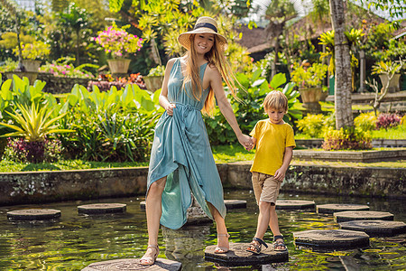 印度尼西亚巴厘岛 水上宫殿 水上公园的妈妈和儿子游客 带着孩子旅行的概念 儿童友好的地方女士男生建筑学树木花朵花园热带池塘雕刻文图片