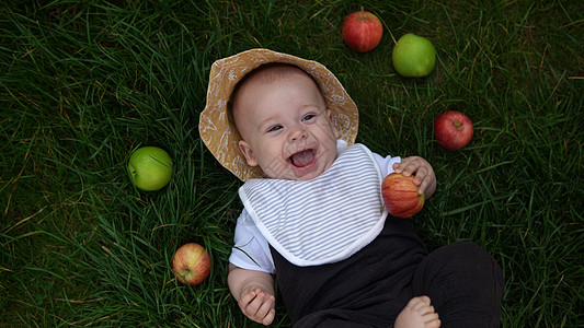夏日巴拿马帽中快乐的新生儿在夏日阳光明媚的日子里赤脚躺在草地上 吃着新鲜水果苹果 婴儿小孩蹒跚学步的男孩在花园里笑脸健康食品自然图片