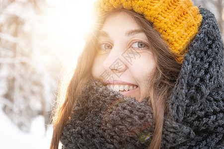 在雪林背景下 一位微笑着的年轻天主教女画像 戴着明亮的羊毛帽和围巾针织帽羊毛天气帽子女士女孩女性森林衣服图片