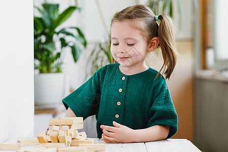 美丽可爱的学龄前女孩在家里玩耍 桌边有木块 自然肥料发育图片