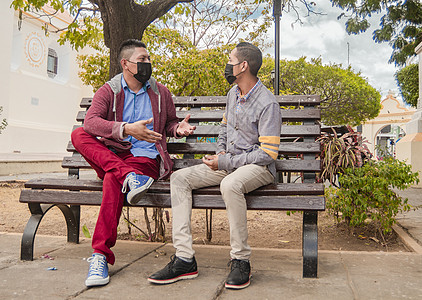 两个戴口罩的男人在长凳上聊天 有社交距离的男人在长凳上聊天图片