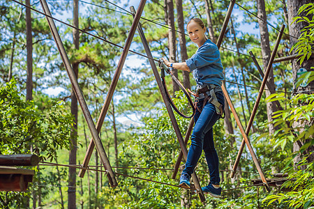 年轻有吸引力的年轻女子在安全设备内冒险游绳公园女士木头娱乐耐力挑战运动自由人心绳索危险图片