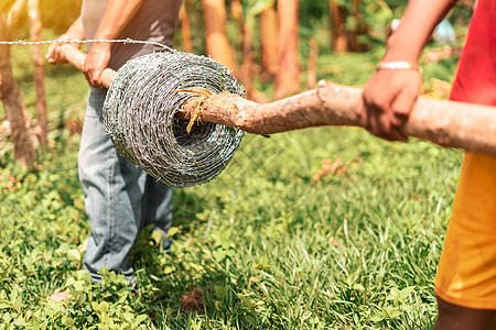 尼加拉瓜两个无法辨认的农民 拿着一卷有刺铁丝圈在一根棍子上背景