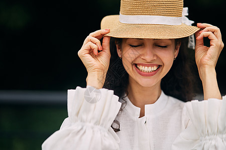 在夏日公园戴帽子的年轻美女微笑衣服草帽日光快乐享受女性青少年阴影成人背景图片