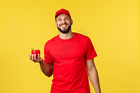 在线交付 购物和食品订单概念 穿着红色制服的红帽子和T恤衫 手持新鲜胡椒 从商店到客户家送菜给顾客家男性工作房子服务社交食物蔬菜图片