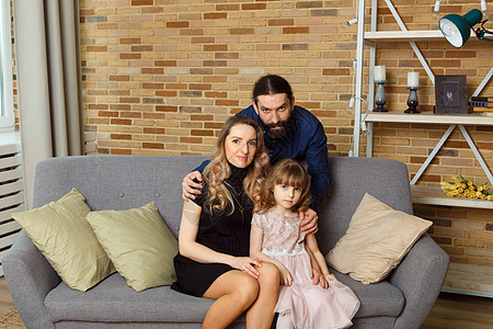 快乐的年轻父亲 母亲和女儿坐在家里的威克沙发上女性父母母性妻子丈夫微笑男性怀孕拥抱沙发图片