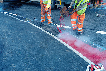 在新建设公路上涂贴热红色道路标识油漆的公路工人修路活动交通施工投资建造路面标记工地安全图片