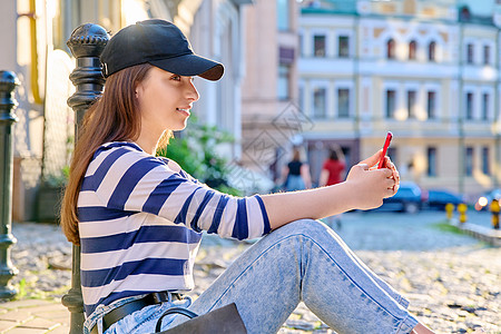 城市风格 流行时尚的少女女性坐在人行道上使用智能手机青少年棒球女孩头发青春期潮人微笑喜悦黑色快乐图片