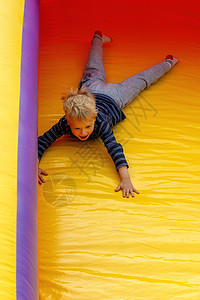 一个快乐的男孩 快速地从一个大而明亮的黄色蹦床上滑下肚子图片