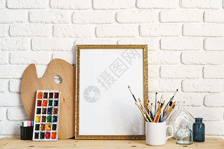 相片框 用画家的工具在木制桌边与白砖墙对齐艺术桌子调色板作坊画架爱好照片画笔装饰风格图片