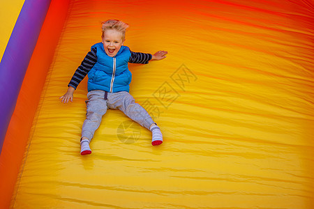快乐的小男孩滑下一个黄色的橙色充气幻灯片 图像中有免费文本空间   info whatsthis图片
