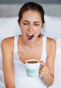 一个大YAWN 年轻女子在床上喝咖啡的时候打哈欠了一下图片