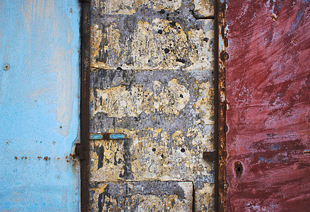 砖块和混凝土粗墙上的蓝色和红色油漆的金属门 形成坚固的抽象纹理背景图片