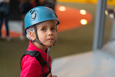 身着蓝防护头盔的可爱小女孩登山者 以及站在攀爬中心儿童游乐园的攀爬渔具学习远足攀岩娱乐岩石女孩风险登山生活方式训练图片