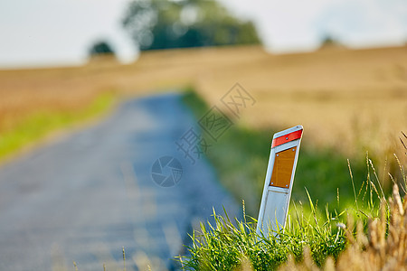 路边反射器特写镜头在路和绿色和棕色草旁边的 夏日道路或街道旁的轮廓标 背景 田野或自然模糊的交通标志图片