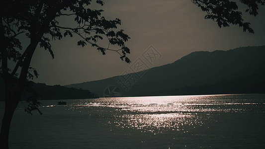 日落时湖面的表面波浪反射出闪光 山底是山地背景橙子时间夕阳阳光太阳森林湖岸山峰公园旅行图片