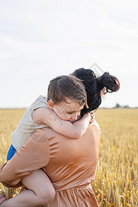 母亲和婴儿幸福家庭在小麦田上行走 拥抱和亲吻女士妈妈父母太阳童年乐趣天空农业闲暇喜悦背景图片