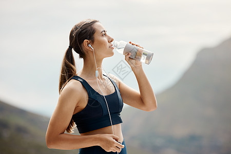 一位健康的年轻混血女性在户外锻炼时休息一下 从瓶子里喝水 女运动员跑步训练后戴耳机解渴降温图片