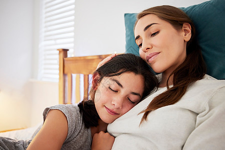 慈爱的母亲坐在床上 十几岁的女儿把头靠在胸前睡着了 年轻的白人妈妈在家里与孩子亲密拥抱并表达爱意图片