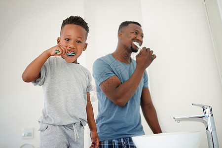 老爸教我怎么刷牙 一个小男孩在家里的浴室里和他父亲一起刷牙的肖像 (笑声)背景图片