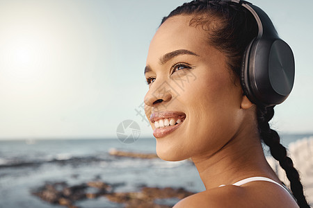 年轻的混血女运动员在沿着长廊跑步时戴着耳机听音乐时看起来很开心和微笑 锻炼身体更健康思维运动装锻炼海滩成人赛跑者闲暇身体女士娱乐图片