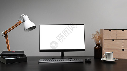黑桌上有空白显示器 灯具 书籍和咖啡杯的电脑图片