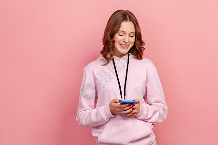 粉红色背景的年轻情感女性的肖像女士露齿冲浪情绪化快乐手机技术闲暇消息风格图片