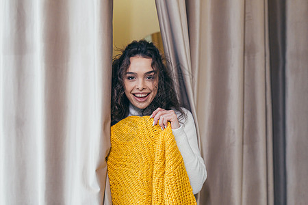 在商场的一家服装店里 一个年轻美丽快乐的女女孩的画像 拿着一个挂着黄色暖毛衣的衣架 带着镜子去试衣间试穿 欢欣鼓舞 微笑 选择 图片