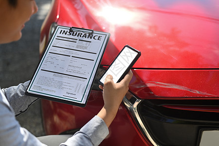 保险代理持有保险索赔表 在检查受损车辆时使用智能电话 (单位 千美元)背景图片