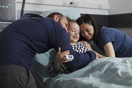 快乐的父母抱着生病的女儿坐在病床上图片