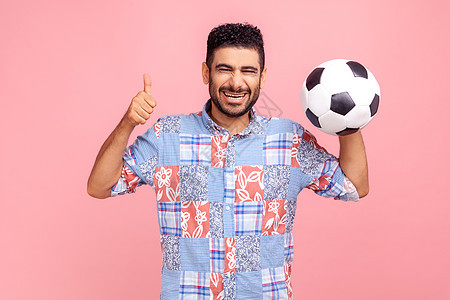 留着黑头发和胡子的快乐兴奋的男人穿着蓝色衬衫摆着足球 竖起大拇指 为足球比赛欢呼游戏高清图片素材