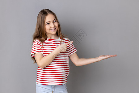 一个女孩肖像小女孩在手掌上展示广告区并指向复制空间的肖像 她被描绘成一个画像背景