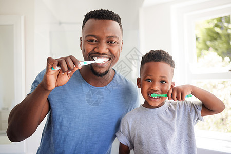 健康的牙齿对您的整体健康很重要 一位父亲和他的儿子在家里的浴室里一起刷牙的肖像图片
