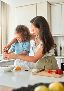 快乐的母亲教小女儿在家厨房做饭 在妈妈做沙拉时把调制的胡椒研磨机加到碗里去女孩父母桌子家庭烹饪房子成人帮助孩子们青年图片