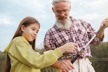 一家人野营老年男子和他的孙女一起钓鱼渔夫资历童年娱乐家庭教学钓竿享受学习幸福背景