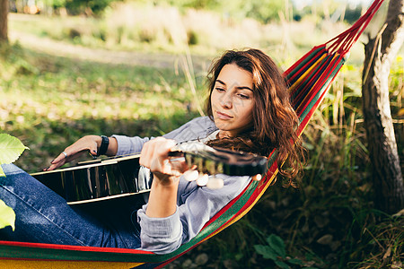 一家人野营年轻美丽的女士在自然中休息 躺在吊床上 弹吉他 唱歌 露营 度假乐趣森林太阳活动假期目的地旅行阅读摄影成人背景