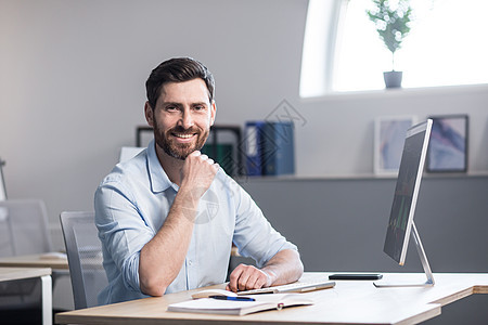 一个年轻英俊男人的肖像 坐在白人办公室的电脑桌前人士员工商务电脑管理人员工作相机桌子自由职业者微笑图片