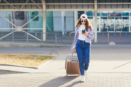 年轻漂亮的女孩 带着手提箱和电话 打电话给某人 找寻呼唤的幸福太阳镜手机飞机场女性游客长发商务休闲运输图片